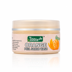 A jar of Tibbi Orange Peel Scrub Wash with a beige-colored scrub visible inside, a light pink label featuring an orange slice graphic, and a translucent cap, set against a clean white background with a soft reflection.