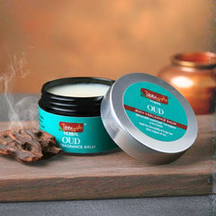Herbal Oud fragrance balm with open lid on a wooden surface, surrounded by oud resins and a candle.
